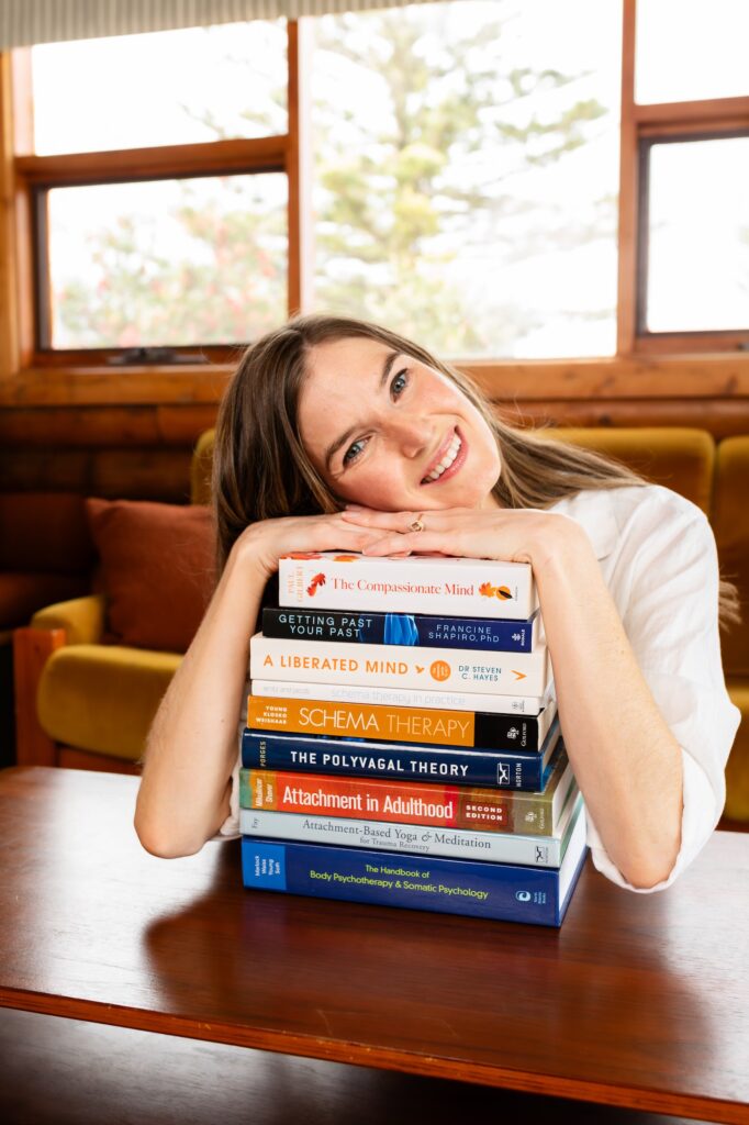 Dr Kaitlin resting her head on a stack of psychology books while smiling